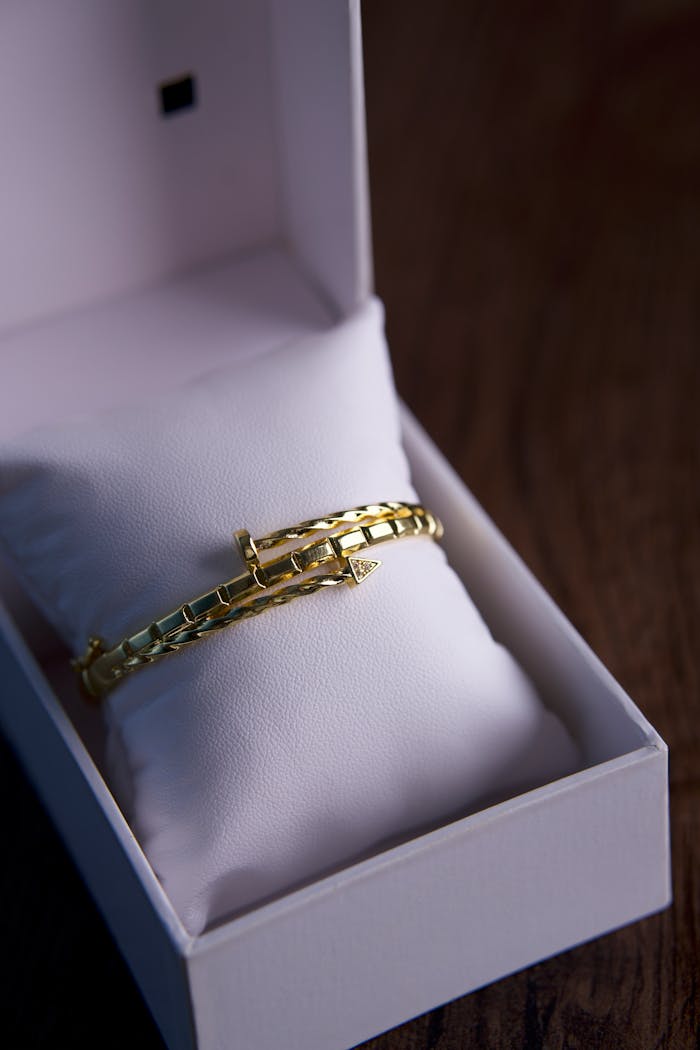 A close-up of a luxurious gold bracelet elegantly displayed in an open gift box on a wooden surface, showcasing fine craftsmanship.